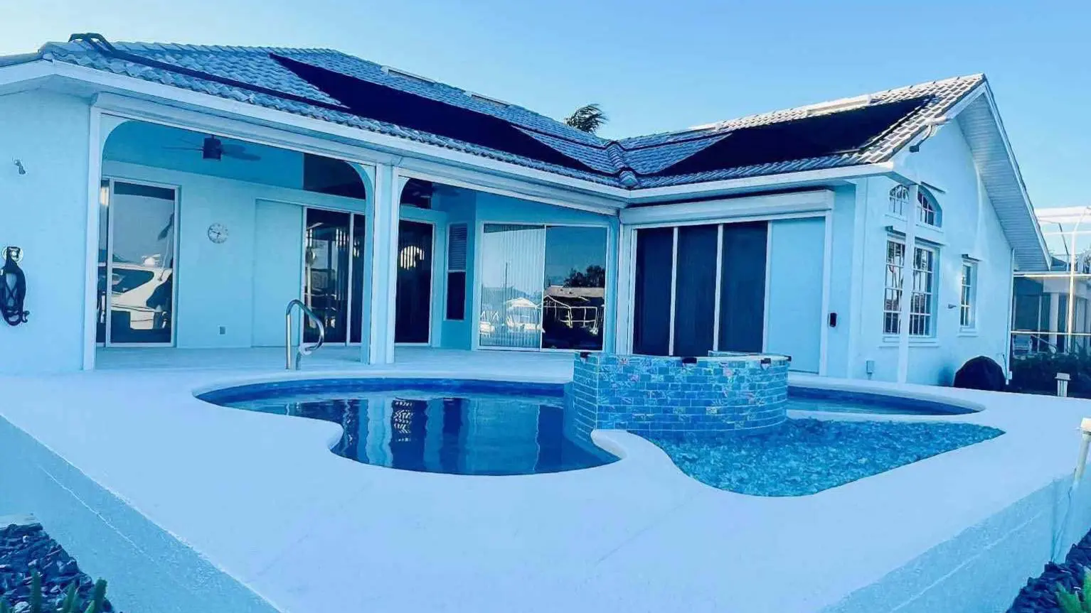 close-up view of a swimming pool edge, featuring bright blue water, a gray granite pool coping with a white plastic overflow drainage grate, and a textured tan interlocking paver pool deck