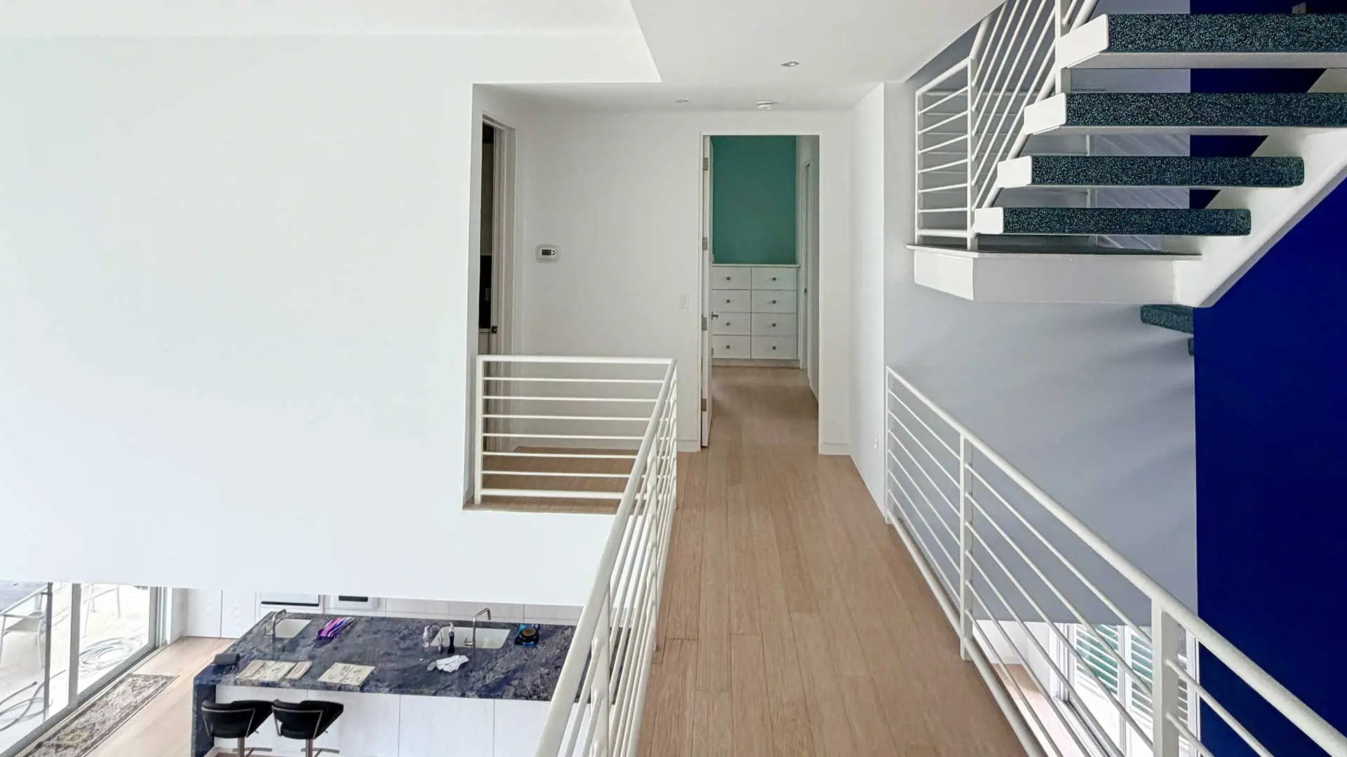 elevated view of open hallway overlooking kitchen and white staircase