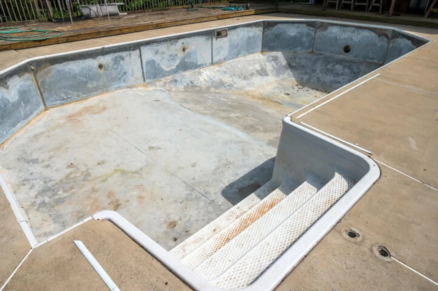 A worn and stained concrete pool deck surrounding an empty pool showing visible deterioration and discoloration.