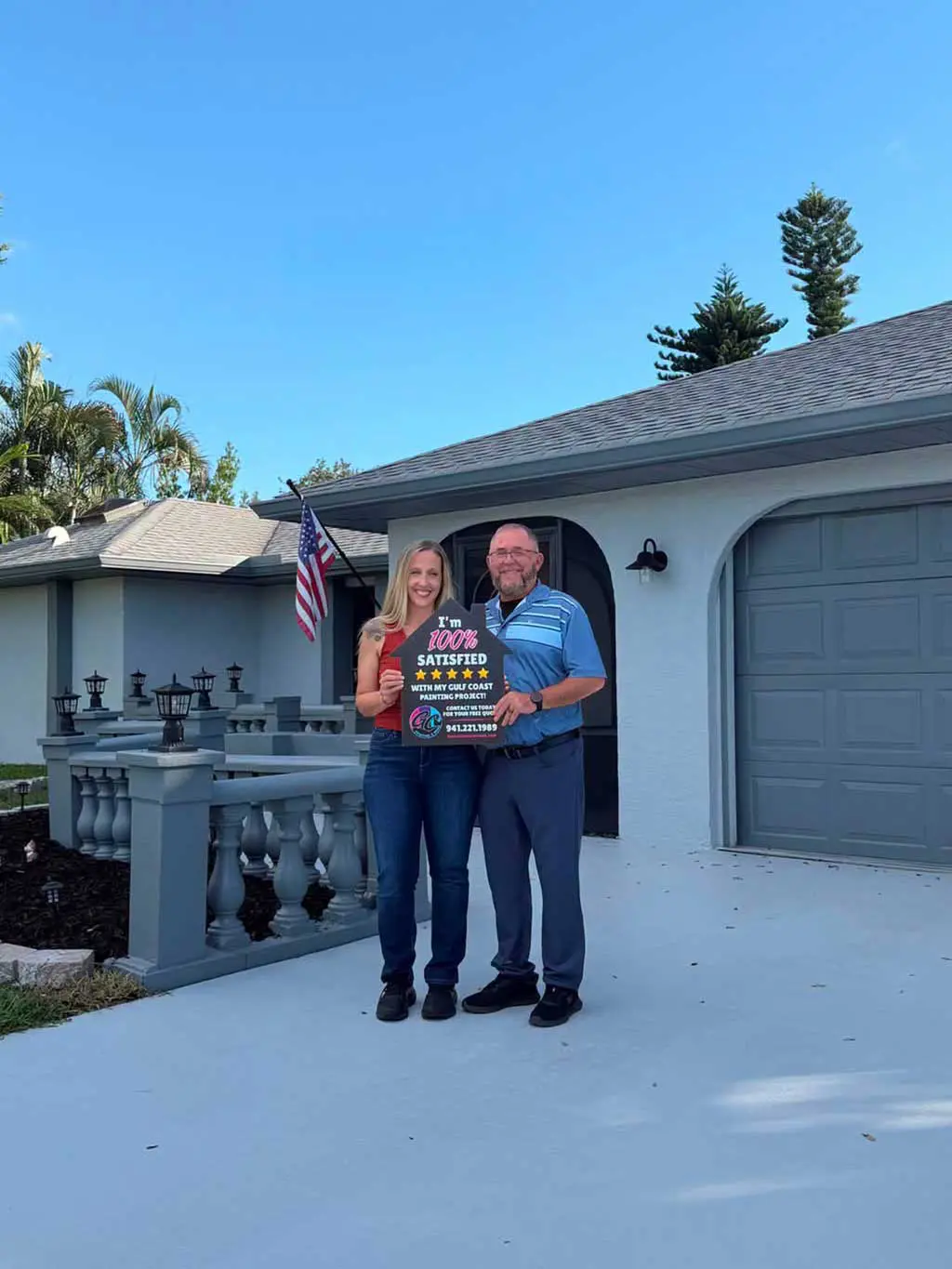 Happy homeowners posing in front of their freshly painted house exterior with a 100% satisfied customer sign