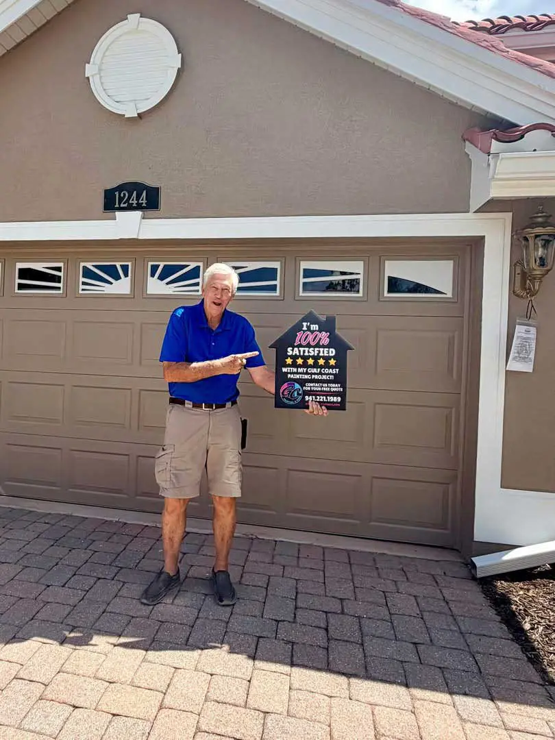 Smiling homeowner standing in front of a newly painted garage door holding a 100% satisfied customer review sign