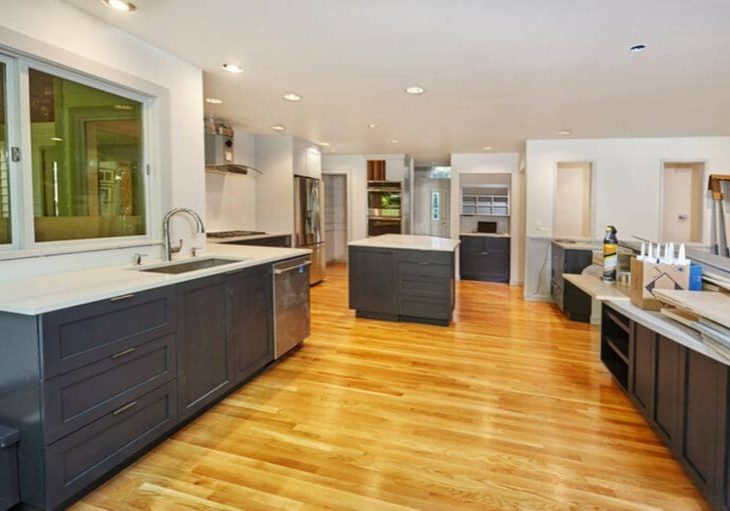 A large kitchen with freshly refinished dark gray cabinets, white countertops, and hardwood floors showing a professional cabinet refinishing result.