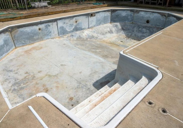 A worn and stained concrete pool deck surrounding an empty pool showing visible deterioration and discoloration.